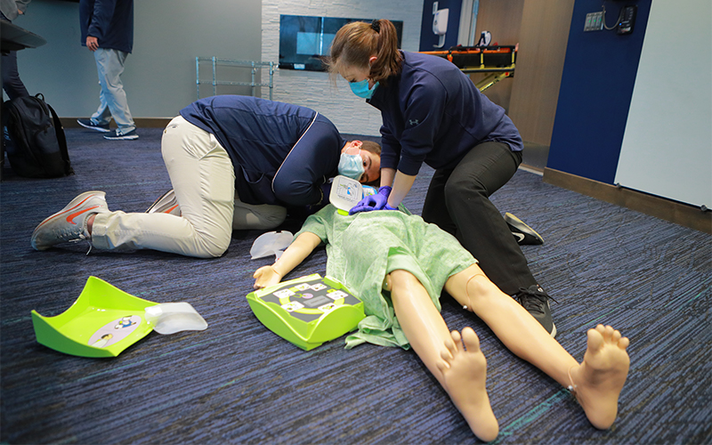 two students practice CPR procedures on a mannequin