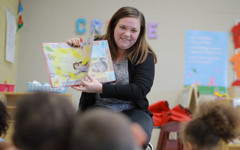 teacher reads and displays a page out of a picture to a classroom of young students