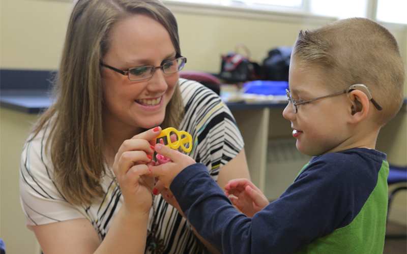 a woman kneels down and hands a young child parts of a toy