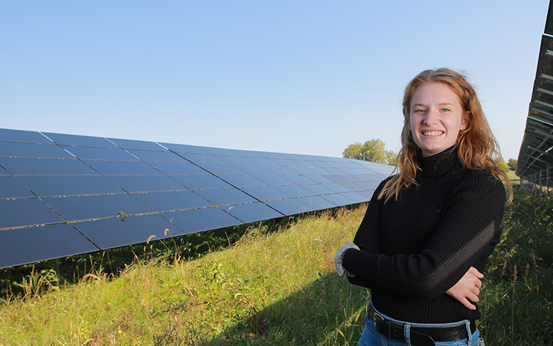 woman in a field stands in front of a row of solar panels