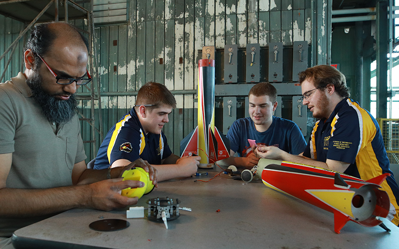 engineering students sit at a table assembling a rocket