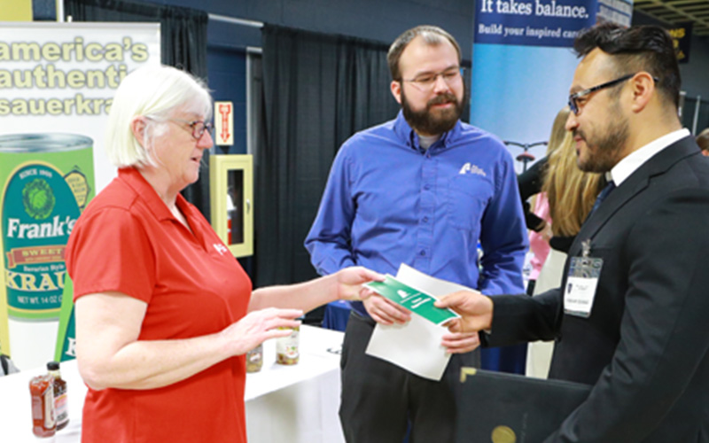 student dressed in a suit talks to two recruiters at a career fair and receives a flyer 