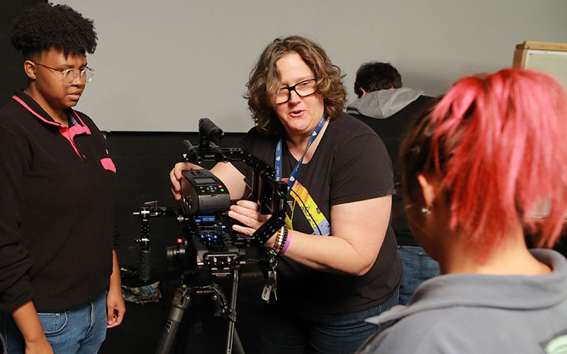 professor assists in angling and adjusting the film camera with two students