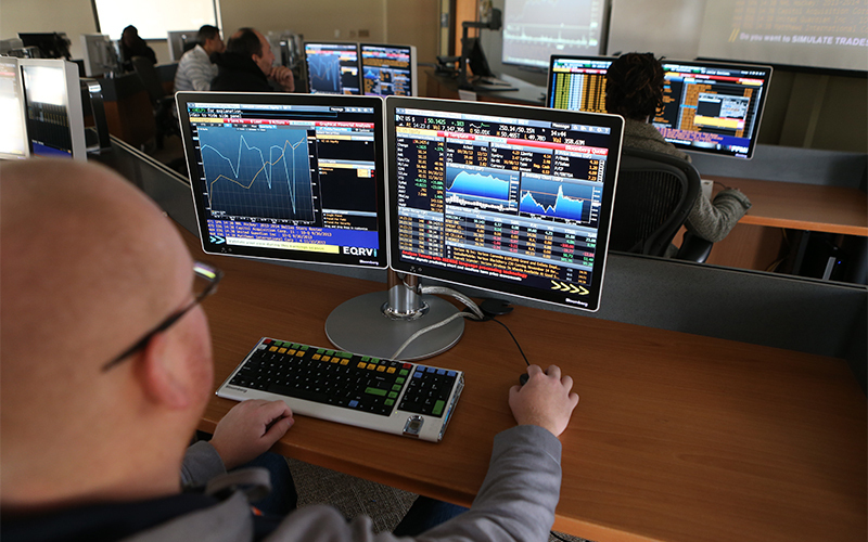 man sitting in front of dual monitor computer screens displaying analytics