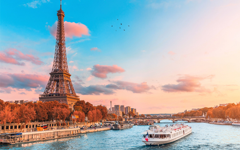 Parisian landscape image featuring the eiffle tower and a ferry boat floating nearby in the river 