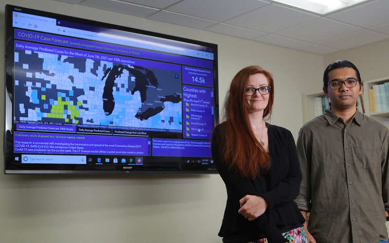 two students stand in front of a screen displaying geographic map data