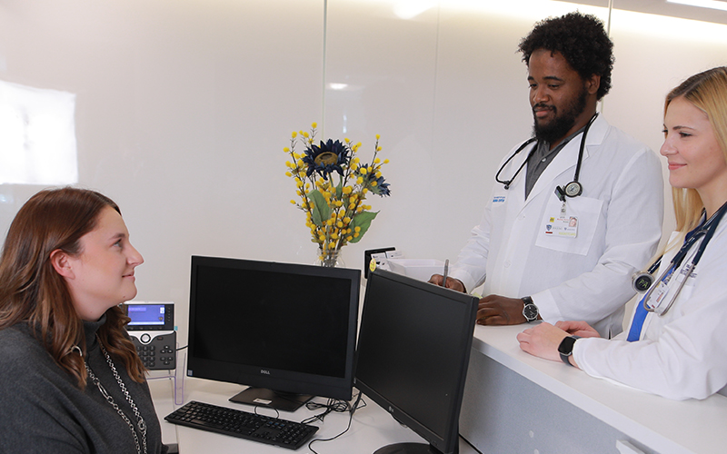two doctors in white coats talk to receptionist sitting at her desk