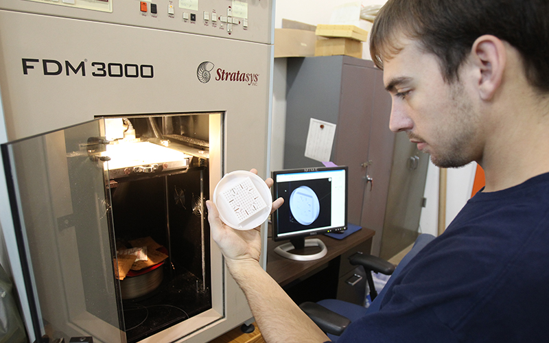man observes a circular white disc removed from a piece of lab machinery