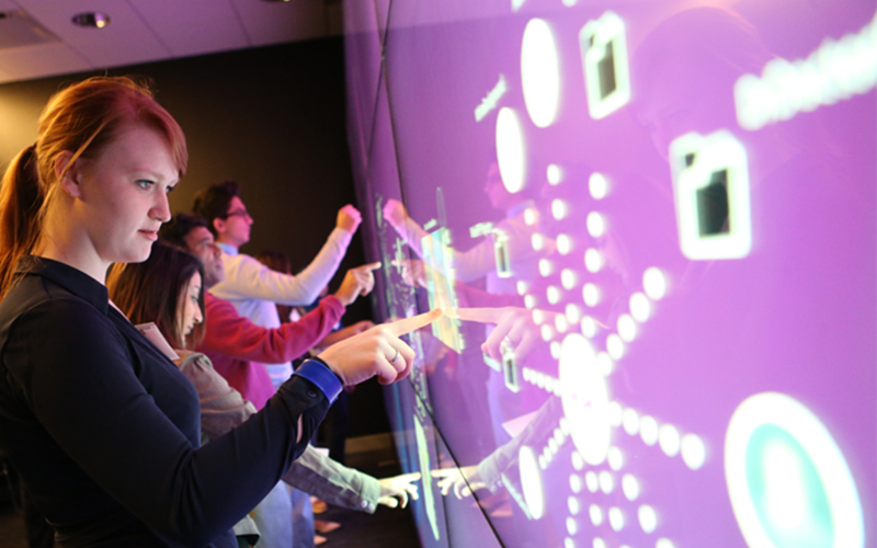 line of students interact with a purple touch screen featuring various elements and buttons