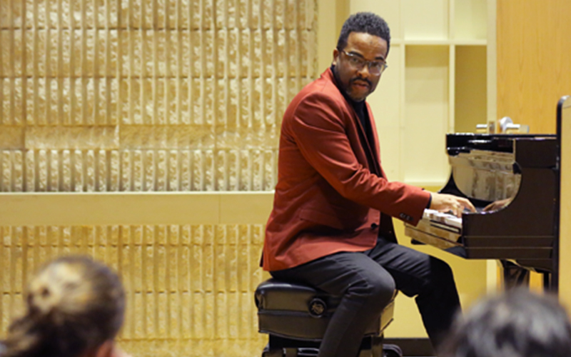 music professor sits at piano in front of class 