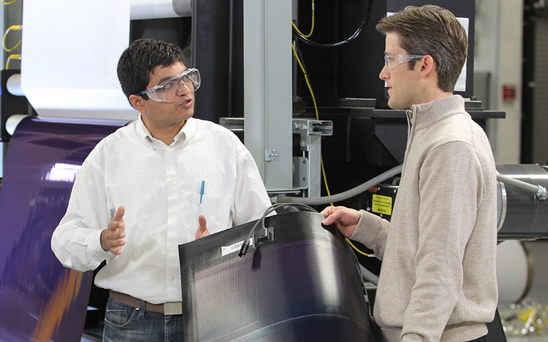two men wearing safety goggles converse in a manufacturing facility