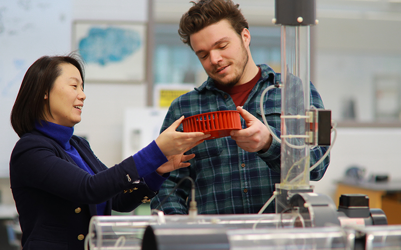 professor presents and hands over a red circular device to student at lab station