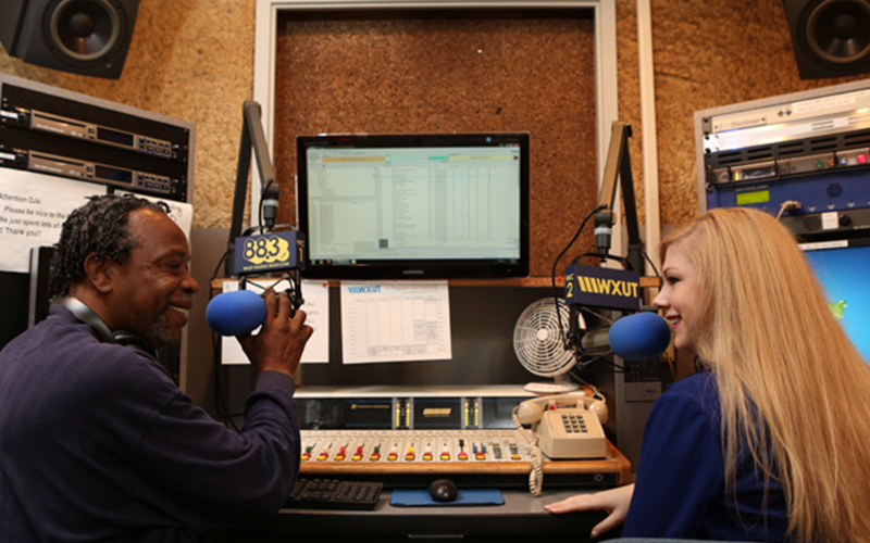 two UToledo radio hosts sit in front of microphones in their radio station