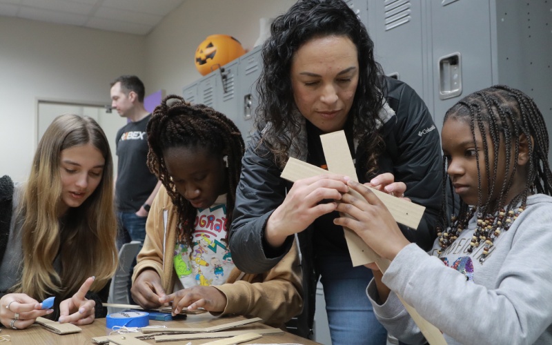 teacher helps assemble a craft along three students