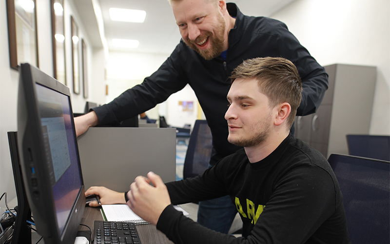 professor and a student wearing an Army shirt observe the content displayed on the computer screen
