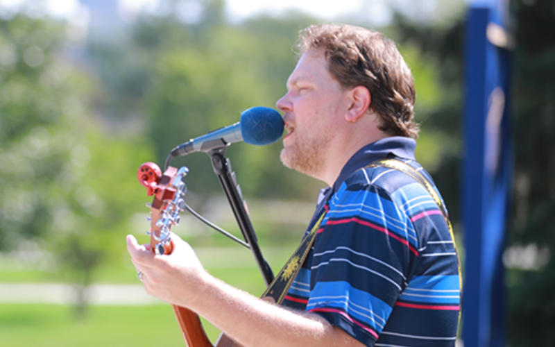 male musician on stage sings into microphone while playing his guitar