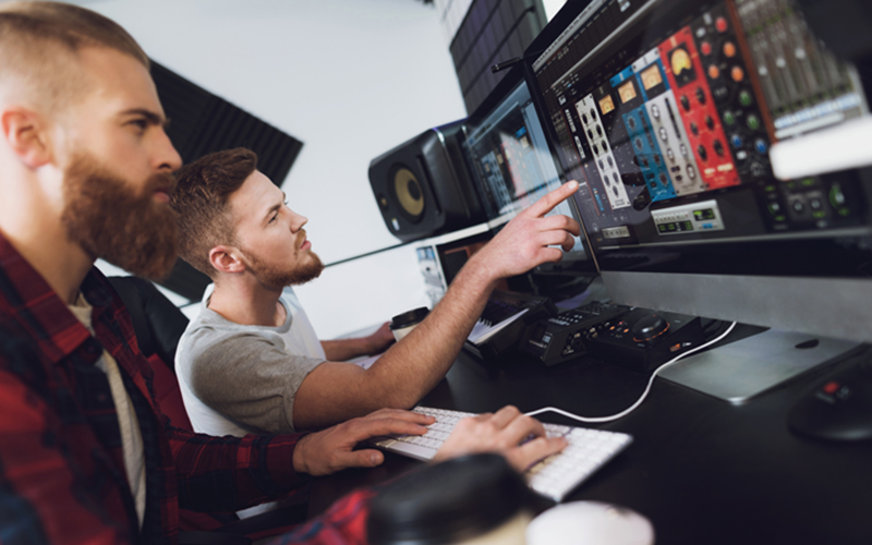 two music artists sit in a studio oberseving a monitor displaying music recording tools and features