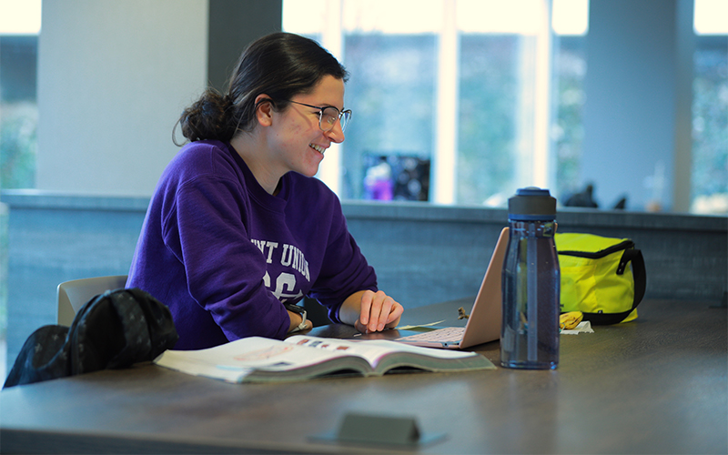 a woman sitting at a table using her laptop and textbook
