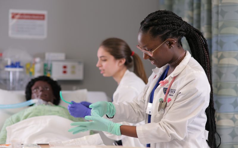 two nursing students provide aid to a medical mannequin