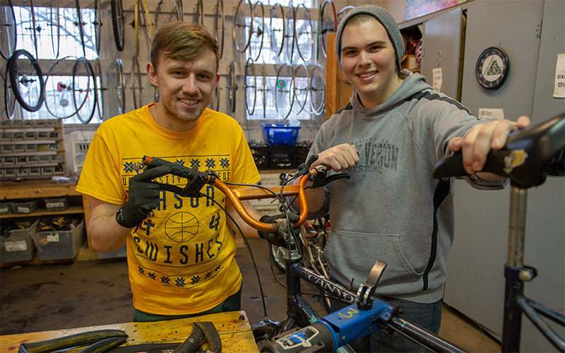 two students smile and stand together in a repair workshop