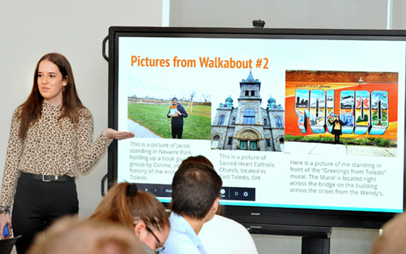 woman presents powerpoint on screen to a group 