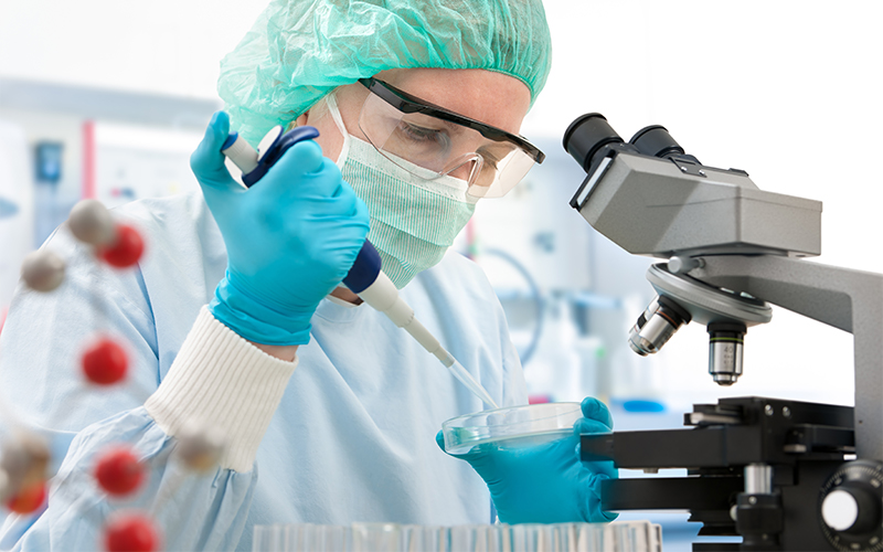 scientist standing in front of a microscope drops liquid onto a test tray for further observation