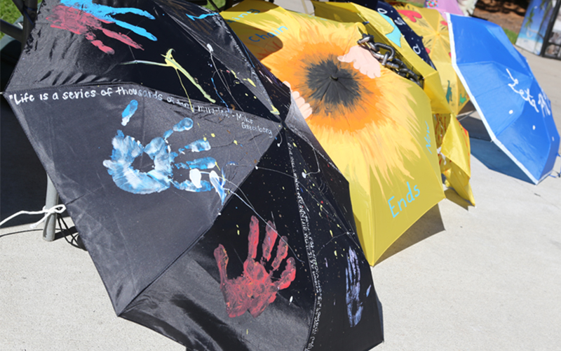 umbrellas lined up on the ground, one is black with colorful handprints