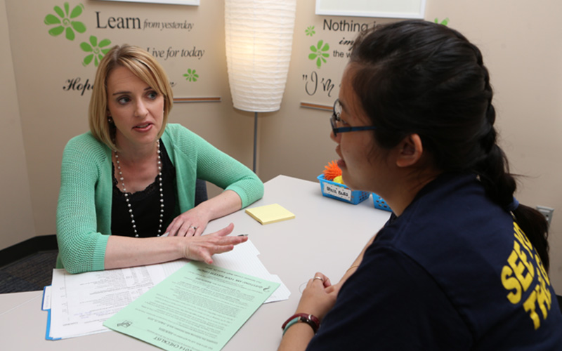 two women sit across from one another at a table with an open file of documents and have a conversation