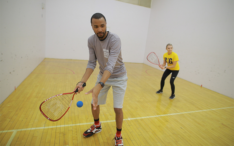 a man and woman in an indoor racquetball court prepare to serve the ball