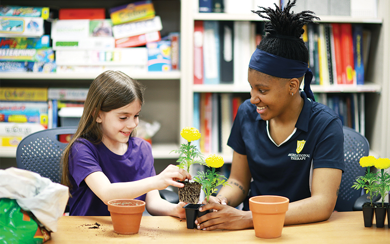 a woman and a young girl planting flowers into small pots