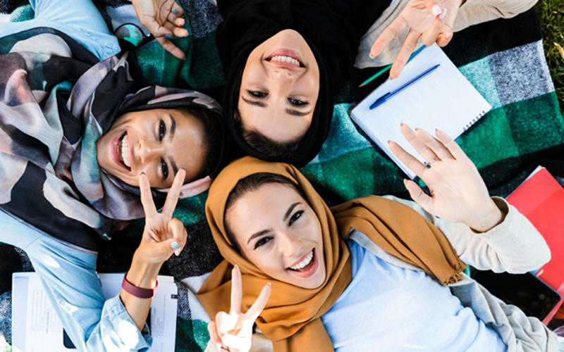 ariel view of three religious studies students smiling and posing with the peace sign to the camera