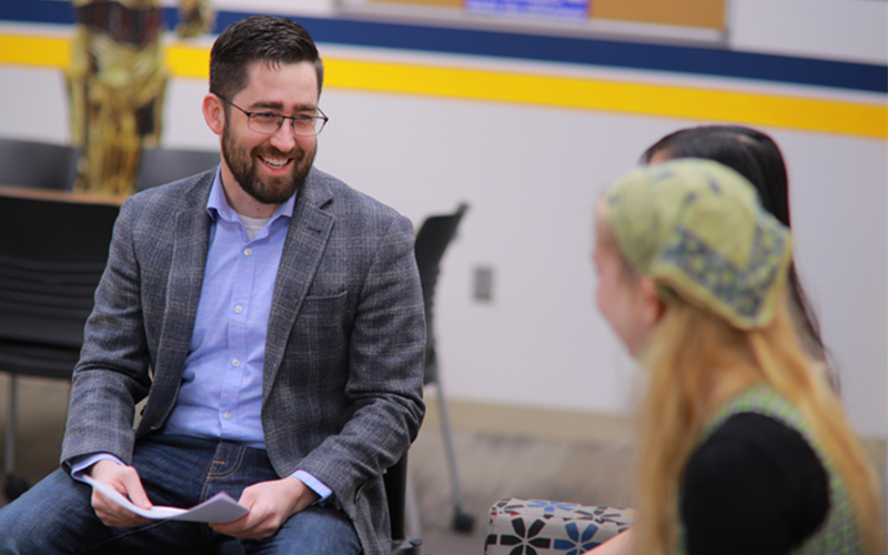 professor engages in conversation and sits with two students 