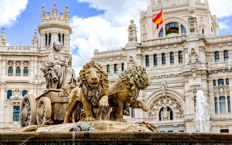 spanish architechture featuring a fountain and flag of Spain waving in the wind