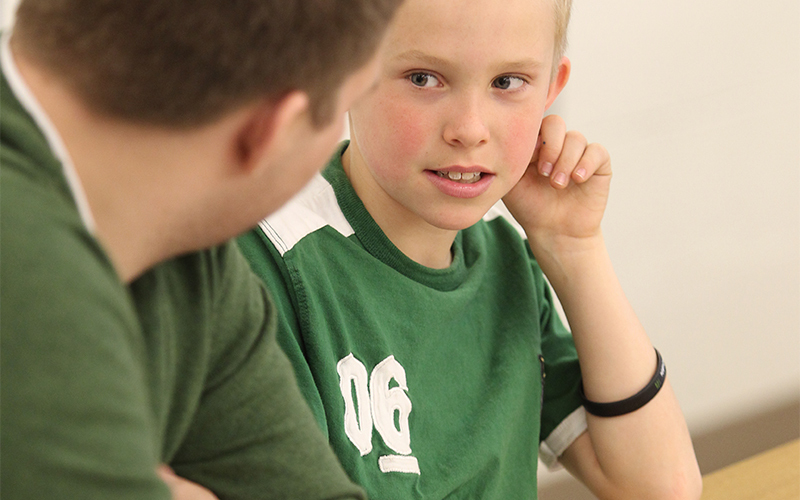 a child sitting besides a man at a table listens in as he speaks