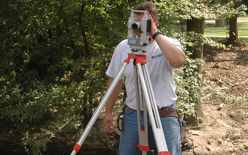man in a wooded area looks through a large camera device 