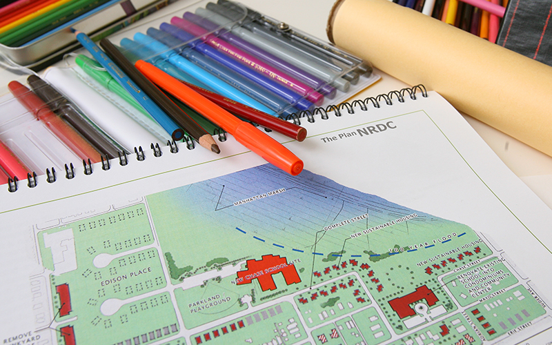 a sketchbook pad with an illustrated map rests next to an open set of markers and pens
