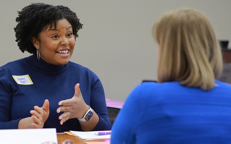 a woman smiles as she engages in conversation with another woman sitting across from her
