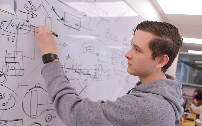 student at a white board examines equations