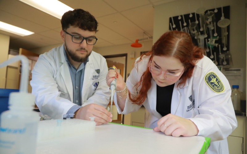 two UToledo Pharmacy students in lab wearing white Pharmacy coats