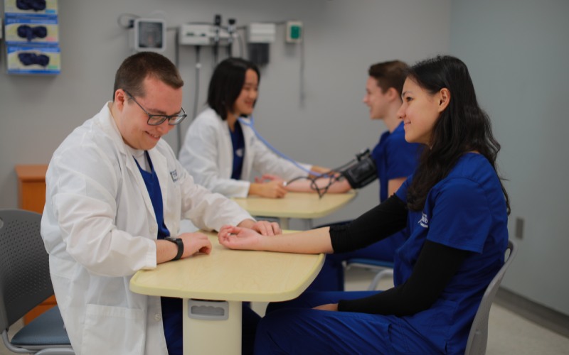 a UToledo student physician seated at a table measures a patient's pulse