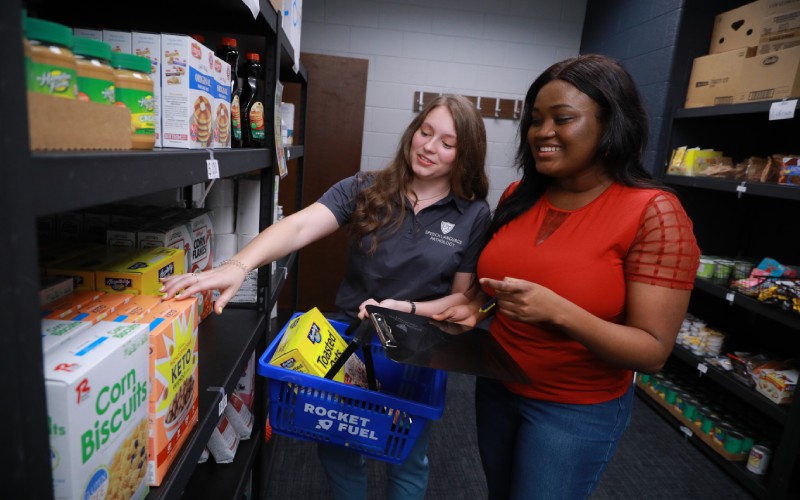 two women pick out groceries from a shelf in a food pantry