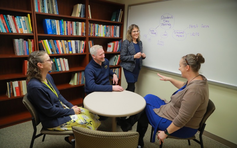 a group sits together at a table for a discussion in front of a white board