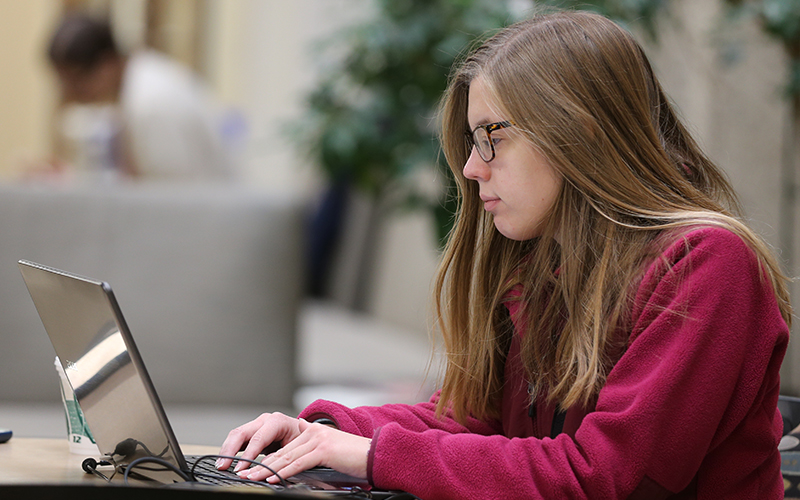 student sitting at a table types on her laptop