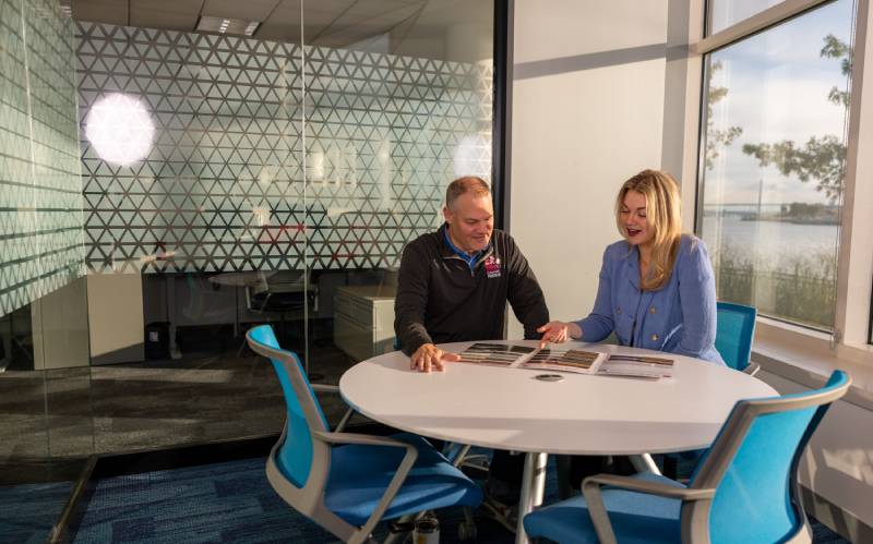 two colleagues sitting at a table nearby a window within a closed conference room office space