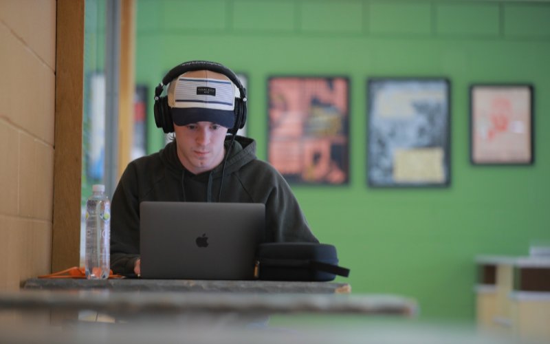student wearing headphones focuses and looks down at open laptop