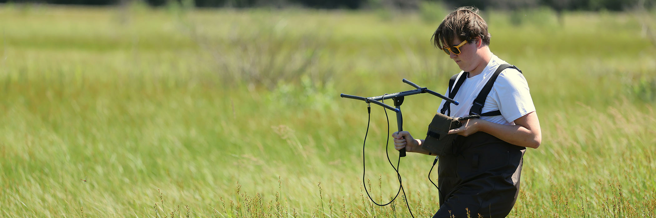 Man out in a field holding a piece of equipment and testing something