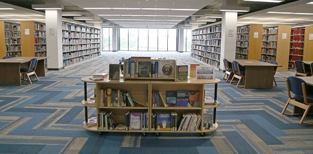 view of library with book display table in front of large window and multiple rows of books in the background
