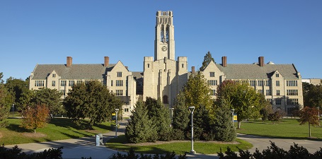 Panoramic view of large building with a clock tower, trees and sidewalks