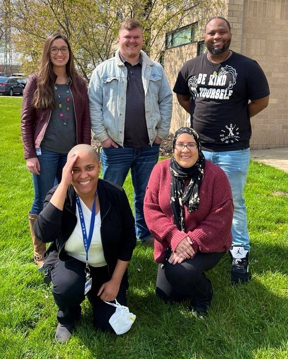 5 people standing in the grass in a formation of 3 standing and 2 kneeling in front of them.