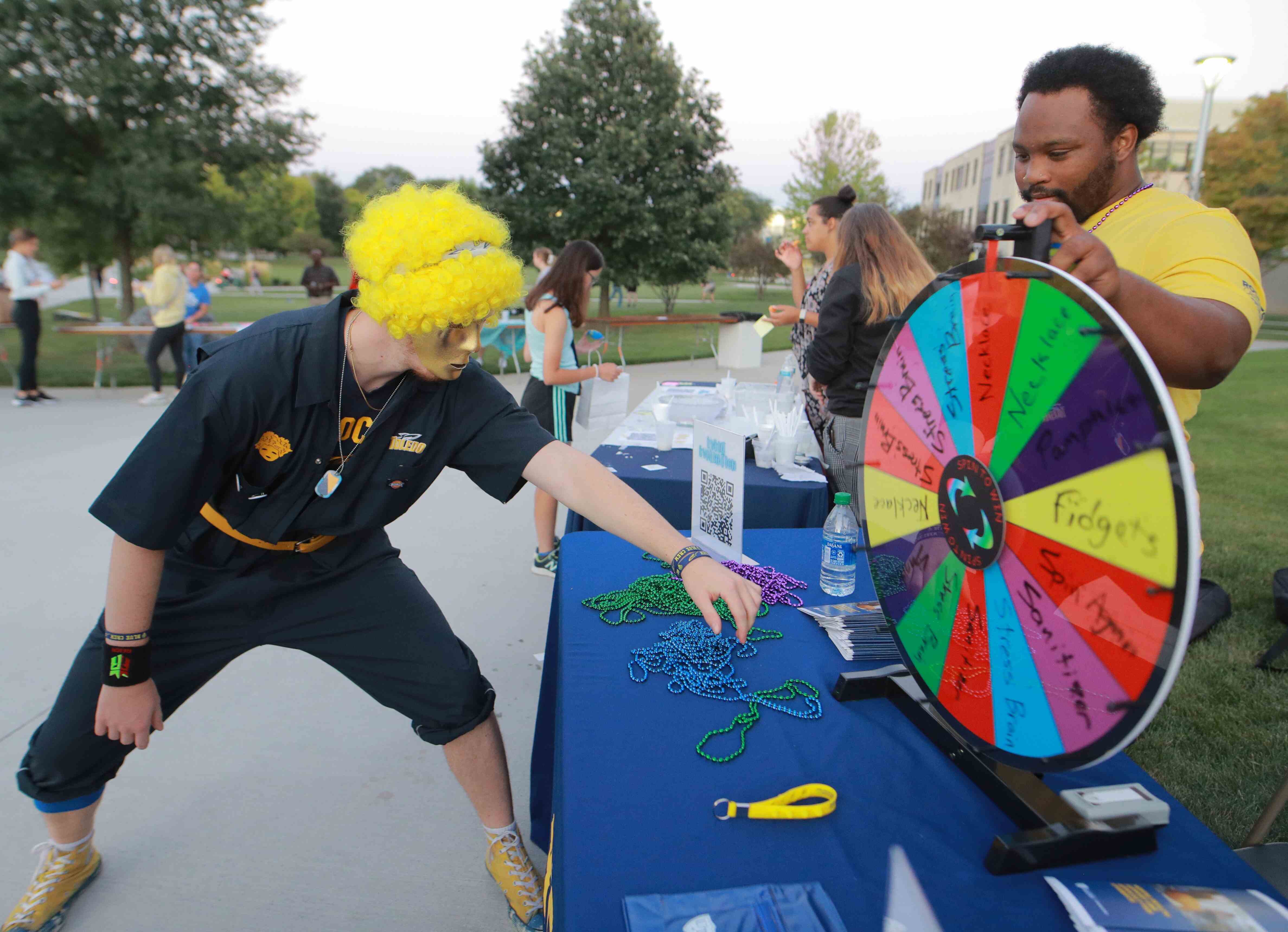 Person dressed in school spirit spinning a prize wheel at an outdoor event.